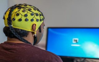 person with electrode cap on head looking at a computer monitor